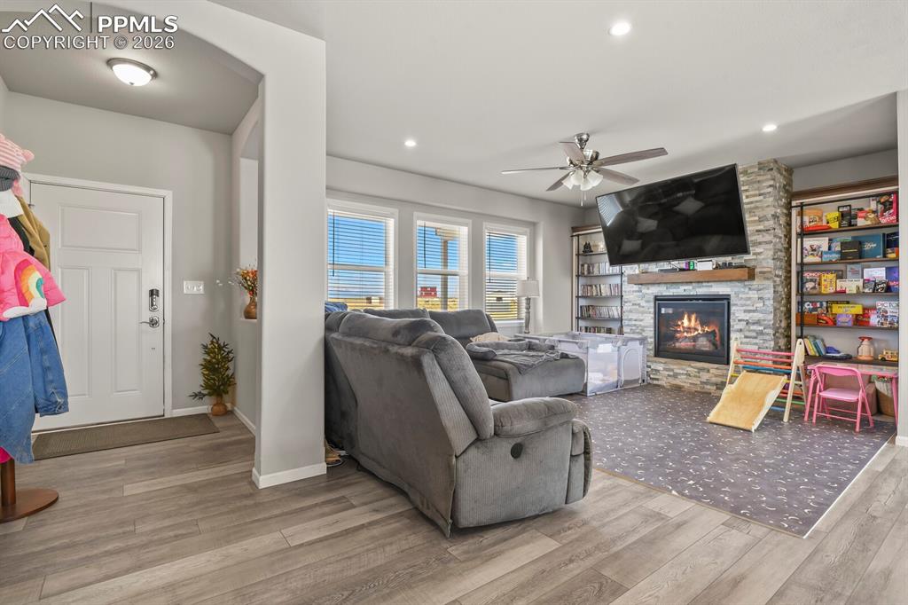 Image 4 of 48: Open-concept living area with wood-finish flooring, a stone-faced fireplace