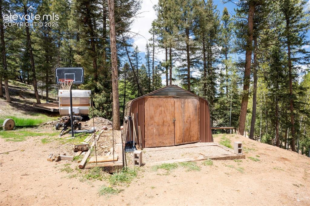 Image 26 of 36: Storage shed with wood panel double doors, situated on a gravel pad