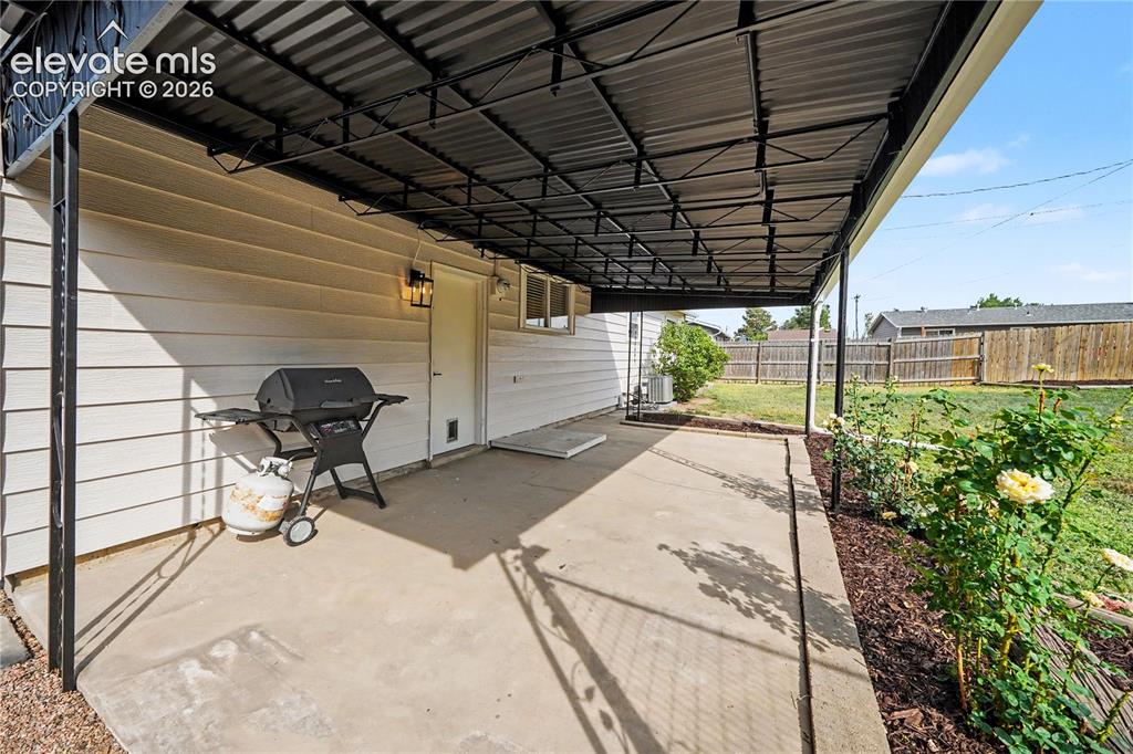Image 15 of 22: Covered concrete patio with white siding exterior, exterior lighting fixtur