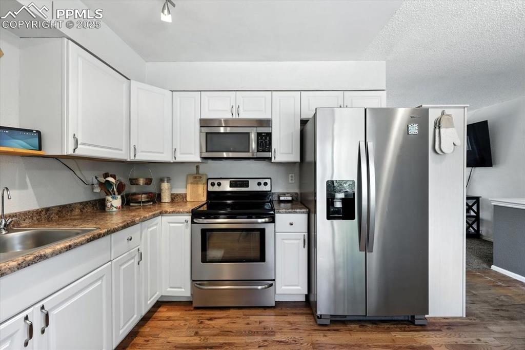 Image 12 of 43: Kitchen with appliances with stainless steel finishes, wood floors, white c
