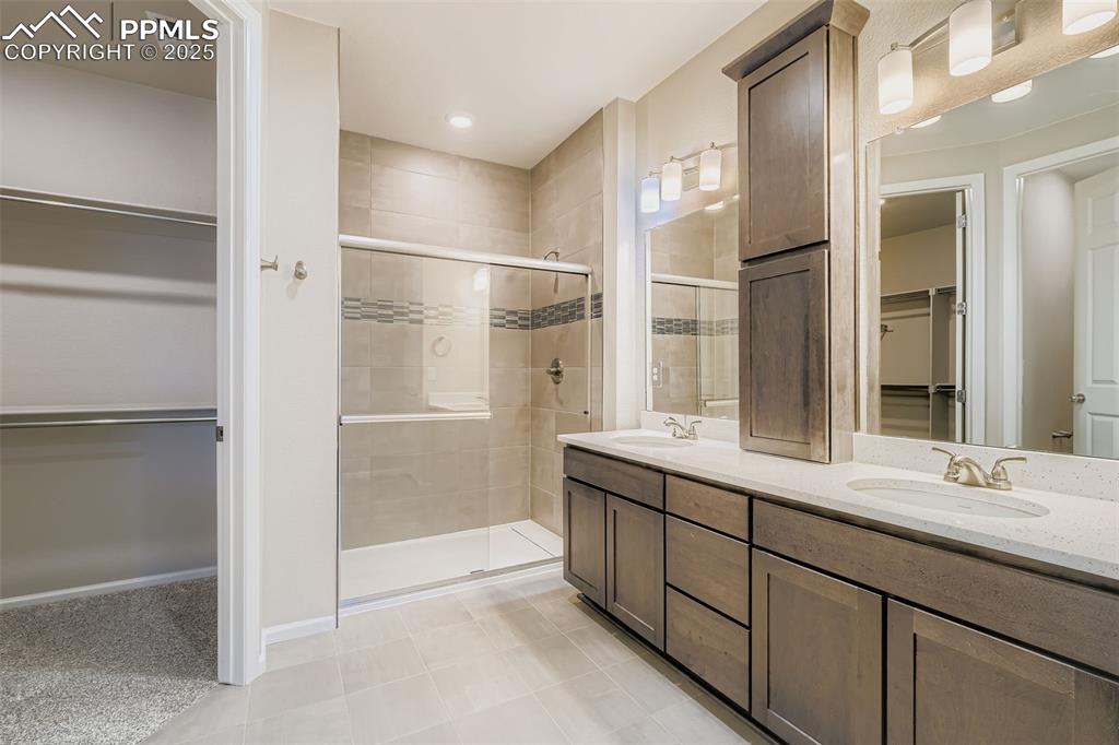 Image 14 of 28: Full bathroom featuring a walk in closet, a stall shower, double vanity, li