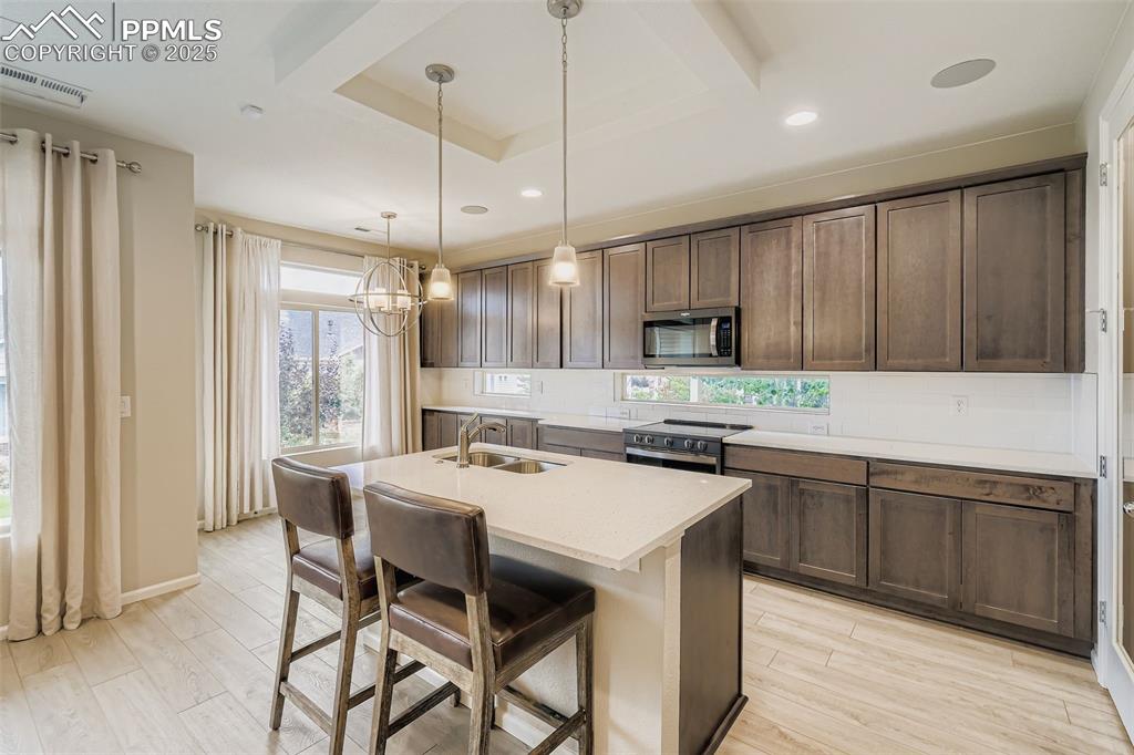 Image 4 of 28: Kitchen with a breakfast bar area, a kitchen island with sink, light wood-s