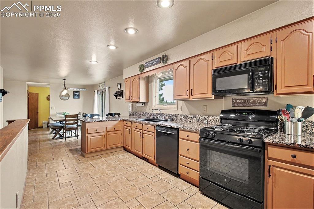Image 11 of 34: Kitchen with black appliances, a peninsula, hanging light fixtures, and lig