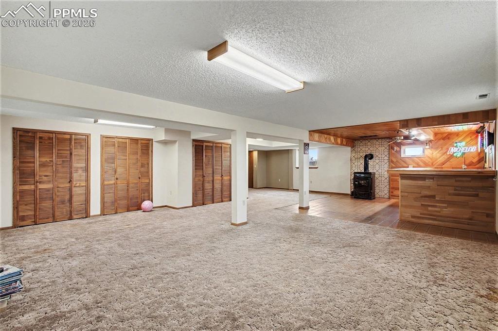 Image 19 of 34: Finished basement featuring wood walls, carpet, a wood stove, and a texture