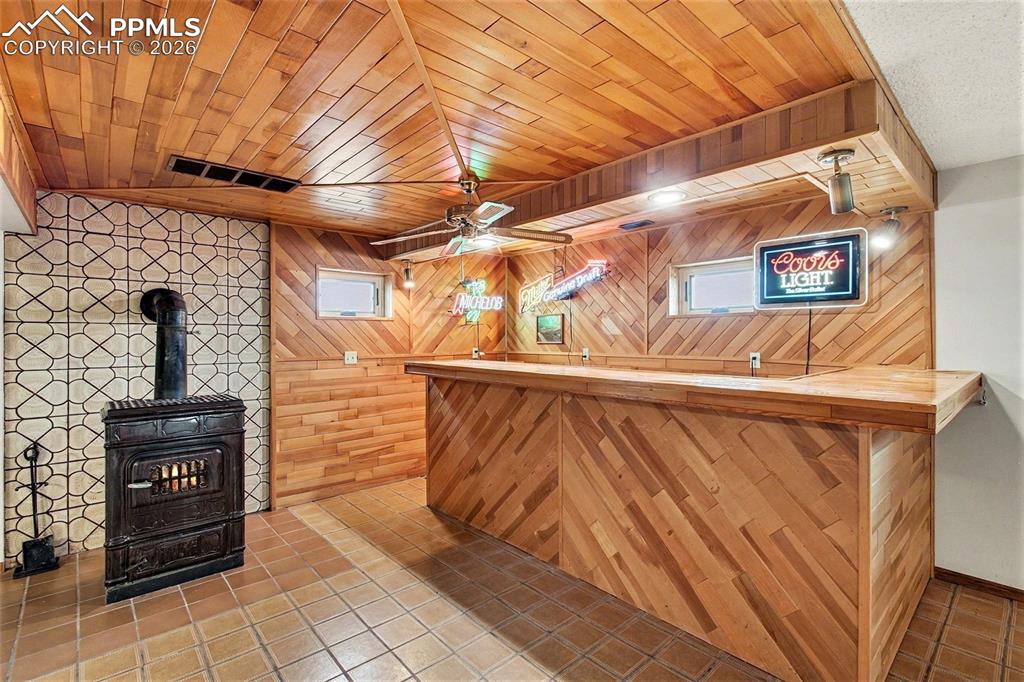 Image 22 of 34: Indoor dry bar with a wood stove, wood walls, tile patterned floors, wood c