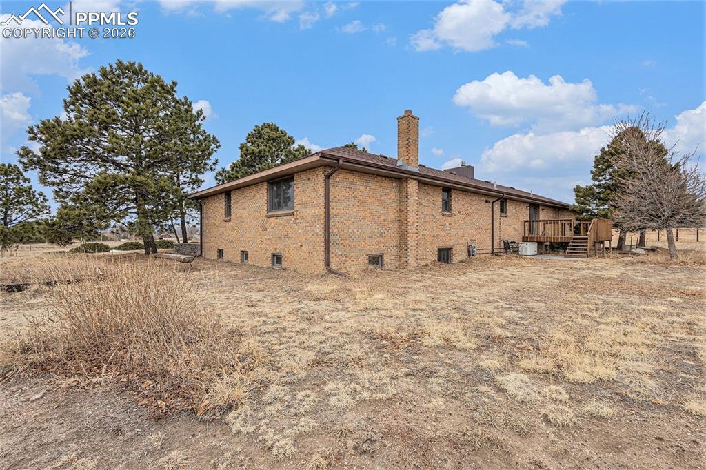 Image 26 of 34: Rear view of house featuring a wooden deck, a chimney, and brick siding