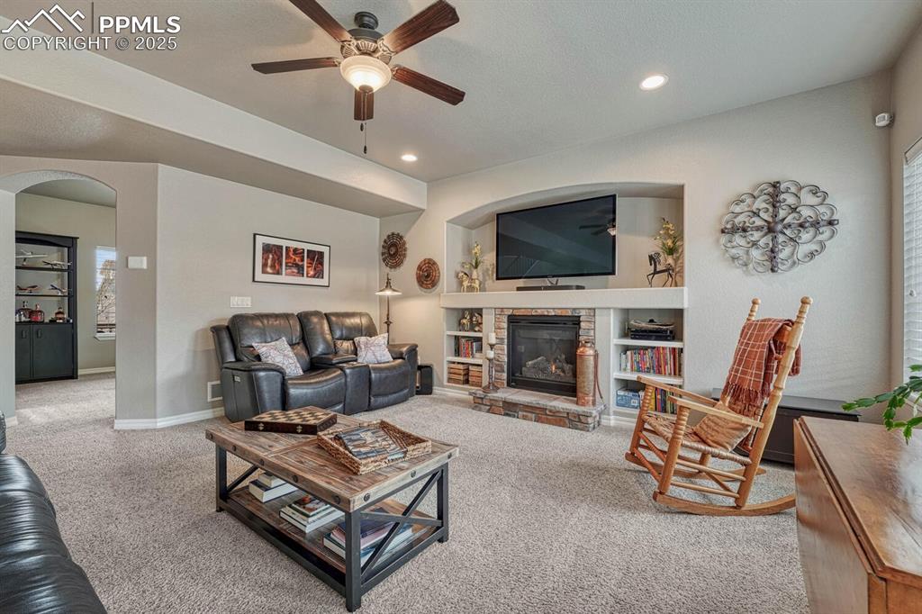 Image 14 of 49: Living room with arched walkways, carpet floors, ceiling fan, and a firepla