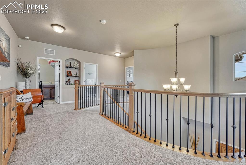 Image 18 of 49: Hallway with an upstairs landing, carpet flooring, a chandelier, a textured