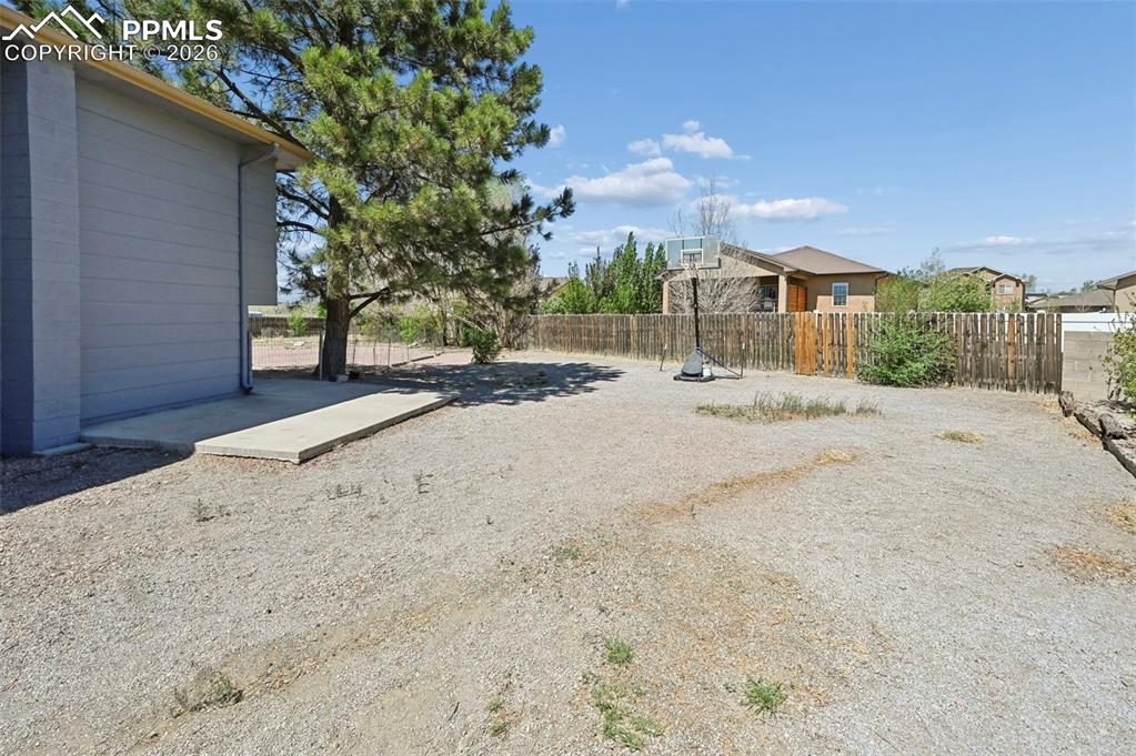 Image 21 of 27: The property features an expansive yard with a mature tree, a concrete pati