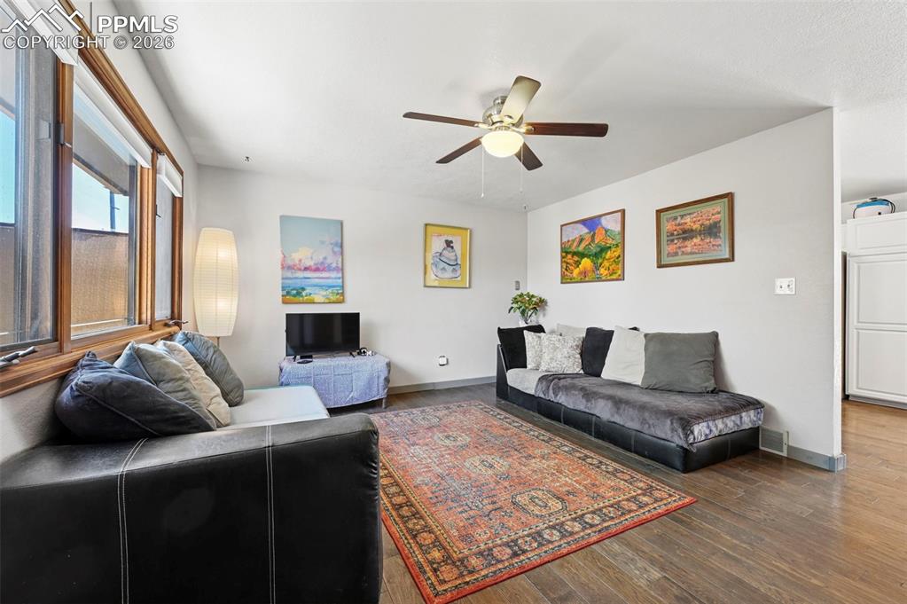 Image 3 of 27: Living area with wood flooring, white walls, and a ceiling fan light fixtur
