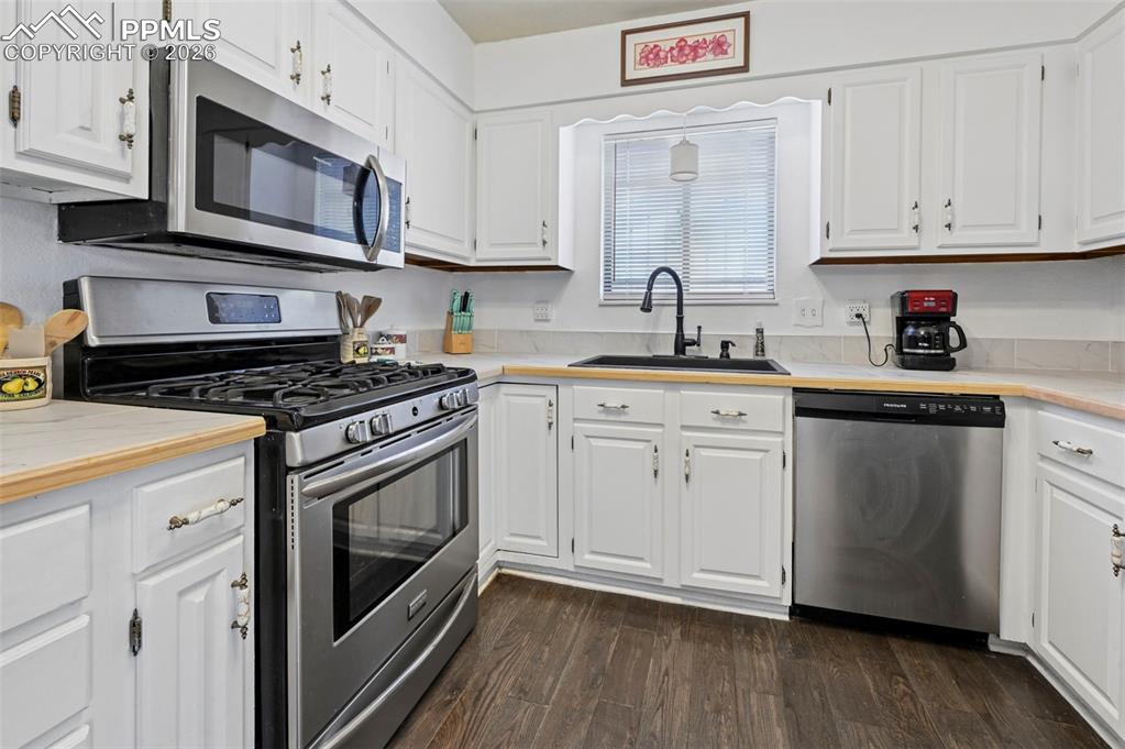 Image 5 of 27: Kitchen featuring white cabinetry, stainless steel appliances, a dark sink 