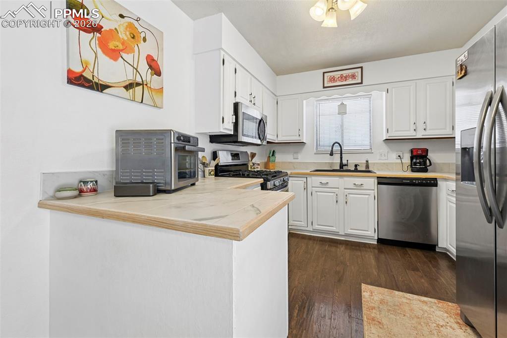 Image 8 of 27: The kitchen features white cabinetry, light-colored countertops, and stainl