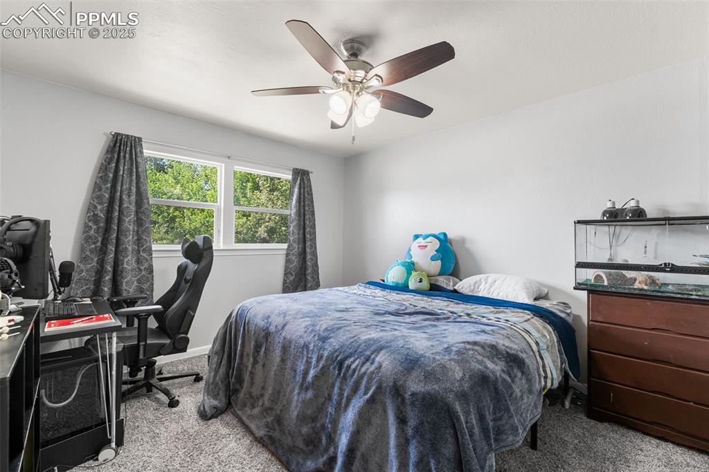 Image 11 of 24: Carpeted bedroom with ceiling fan and a desk