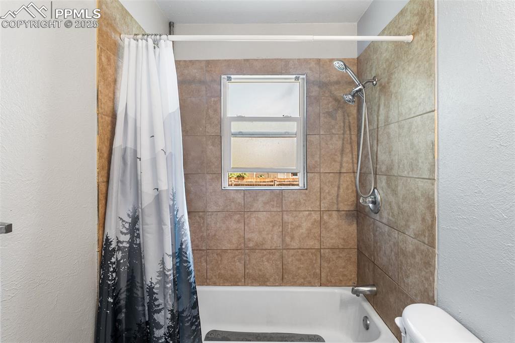 Image 15 of 24: Bathroom featuring shower / bath combo with shower curtain, toilet, and a t