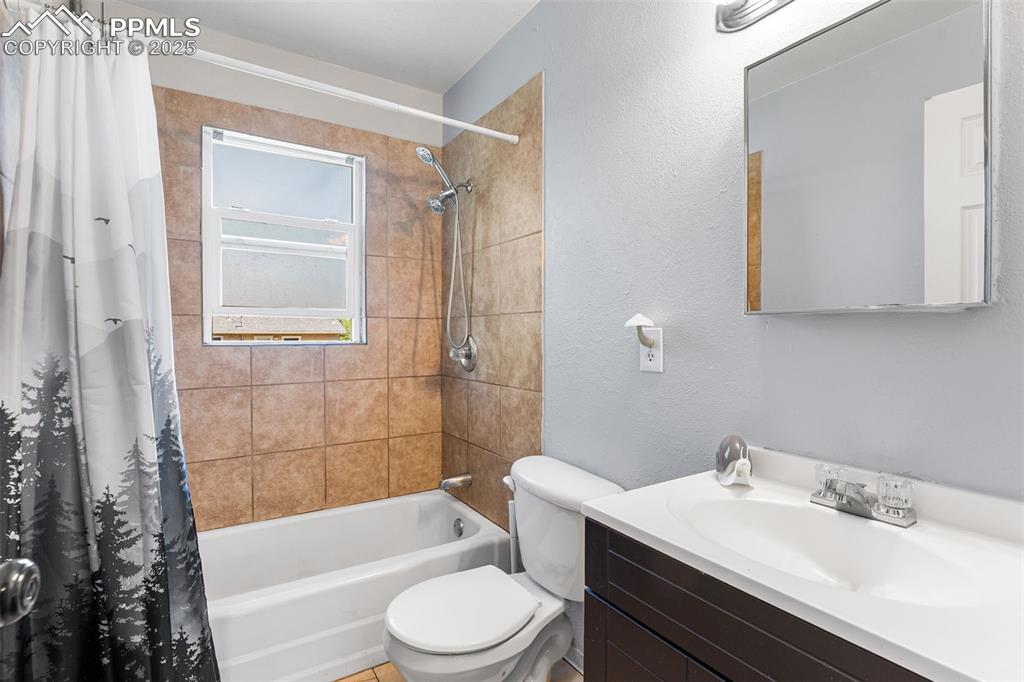 Image 16 of 24: Bathroom featuring toilet, a textured wall, shower / tub combo, and vanity