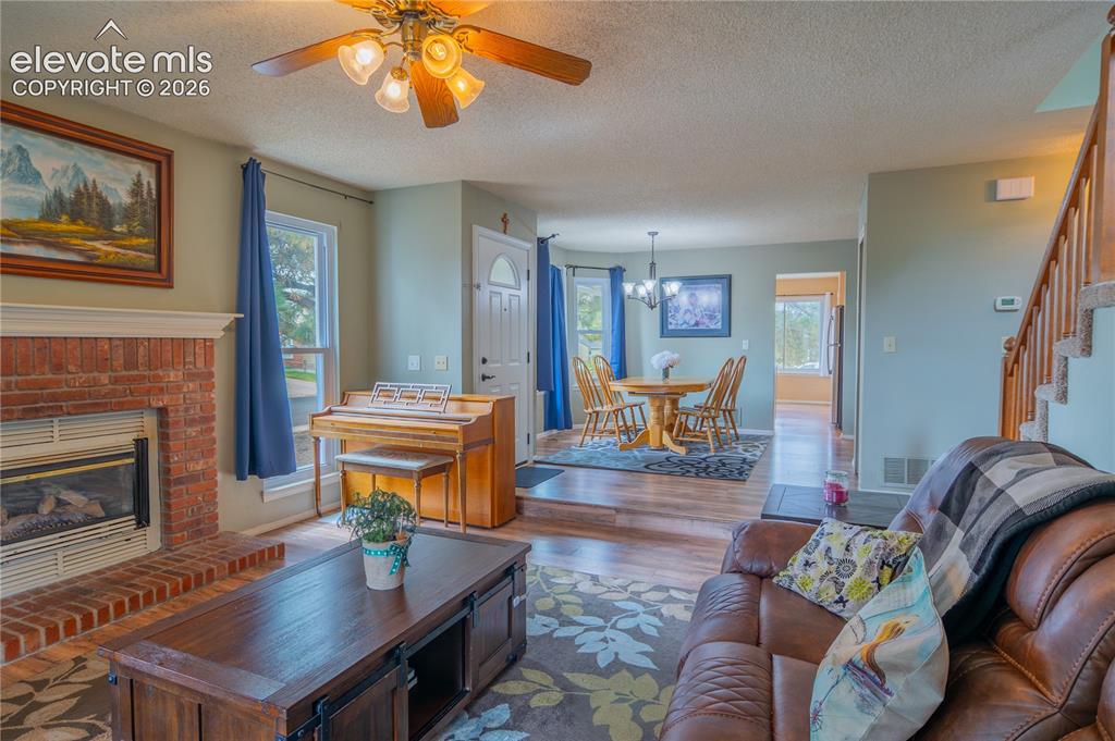 Image 10 of 42: Brick fireplace with hearth, wood-finish flooring, ceiling fan with integra