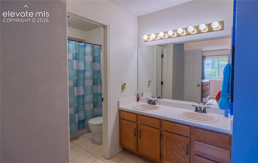 Image 18 of 42: Dual vanity with integrated sinks, wood-finish cabinetry, and a large wall-