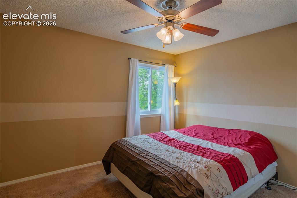 Image 22 of 42: Textured ceiling, ceiling fan with integrated lighting, window with white c