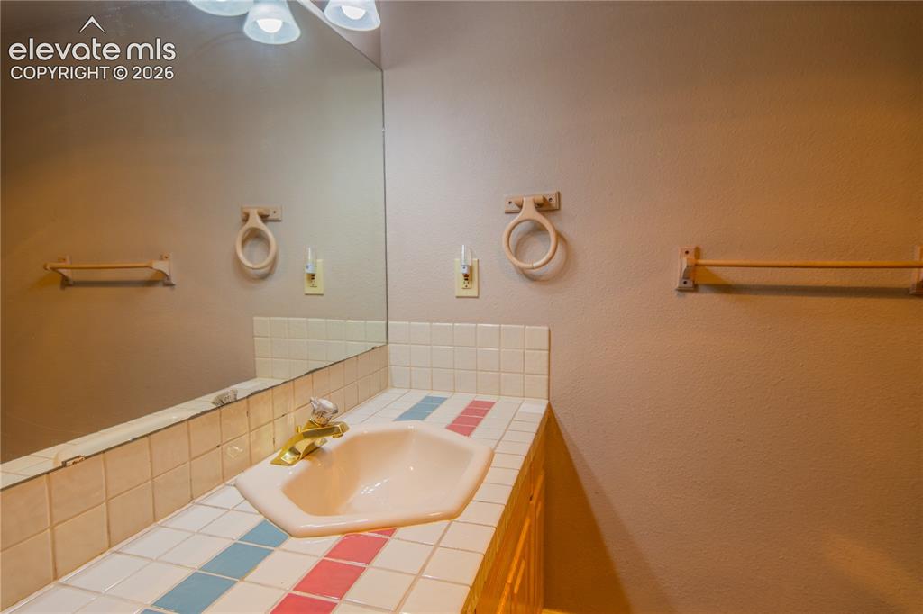Image 29 of 42: Vanity with a drop-in sink, tiled countertop, and a large wall-mounted mirr