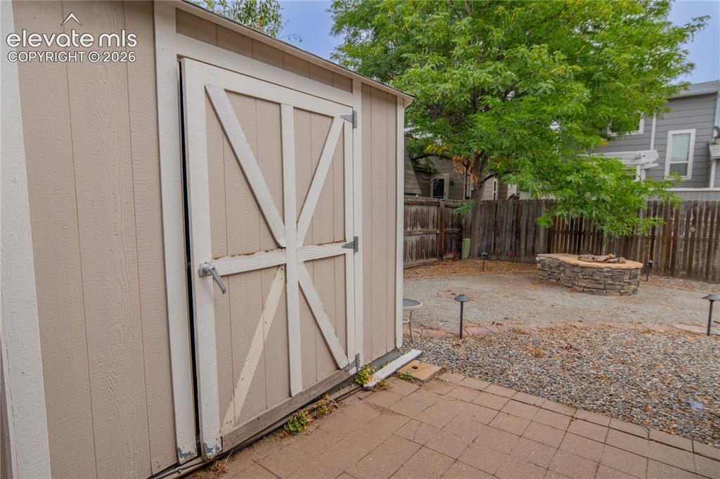 Image 34 of 42: Outdoor storage shed with a panel door, paver patio, gravel yard, and a sto