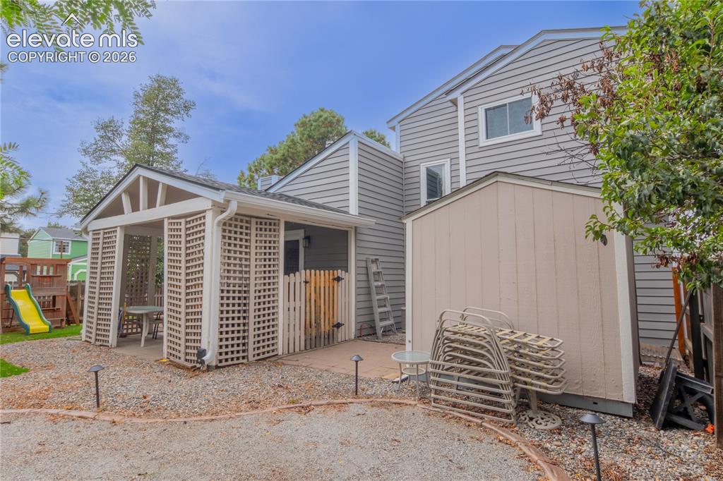 Image 37 of 42: Gable-roofed pergola with lattice walls, gravel patio, and outdoor storage