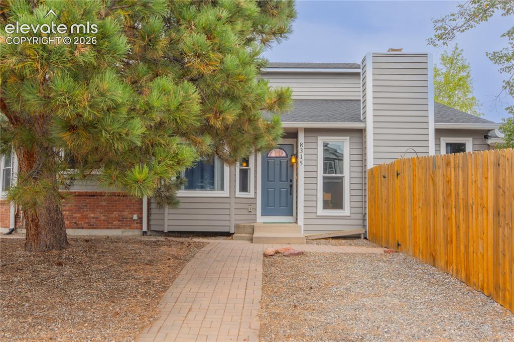 Image 38 of 42: Light gray siding exterior with a dark blue entry door, a prominent chimney