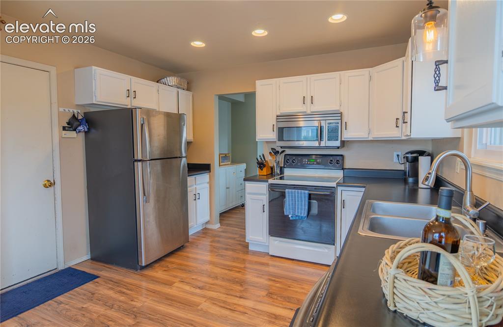 Image 5 of 42: Kitchen with wood-finish flooring, white cabinetry, dark countertops, and s