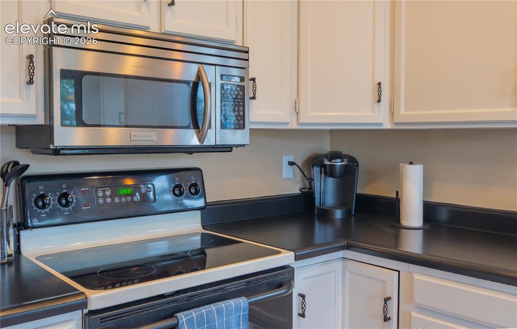 Image 6 of 42: White cabinetry with dark ornamental hardware, black countertops, stainless