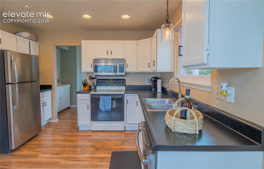 Image 7 of 42: Kitchen featuring white cabinetry, wood-finish flooring, stainless steel ap