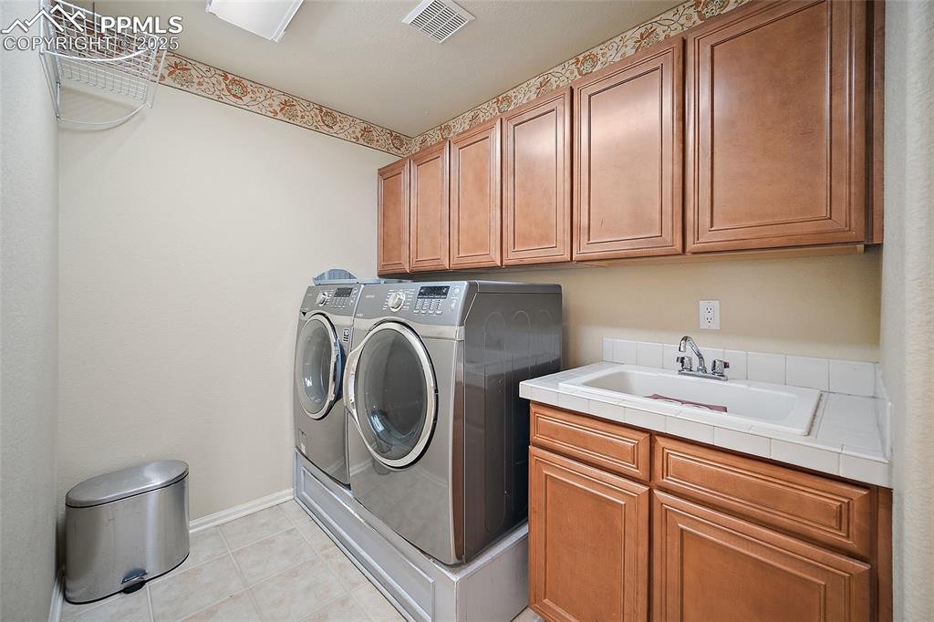 Image 33 of 50: Upper-level laundry with wet sink and plenty of storage. 