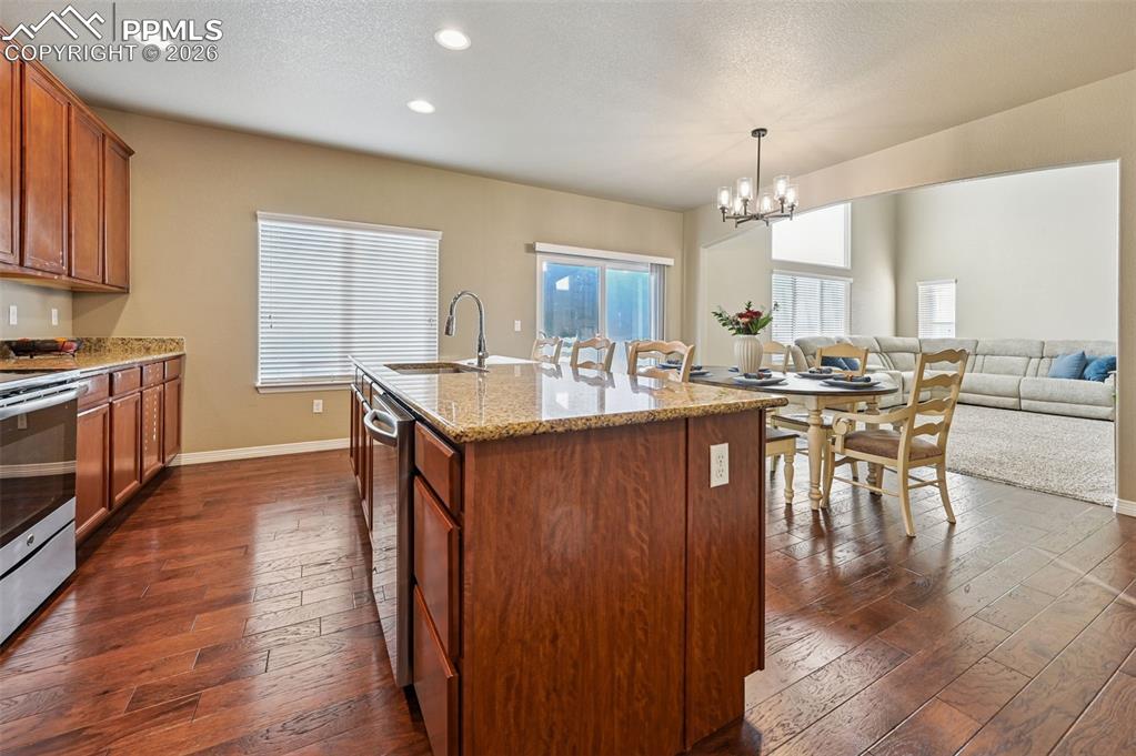 Image 12 of 38: Kitchen with wood finish cabinets, light stone counters, dark wood-style fl