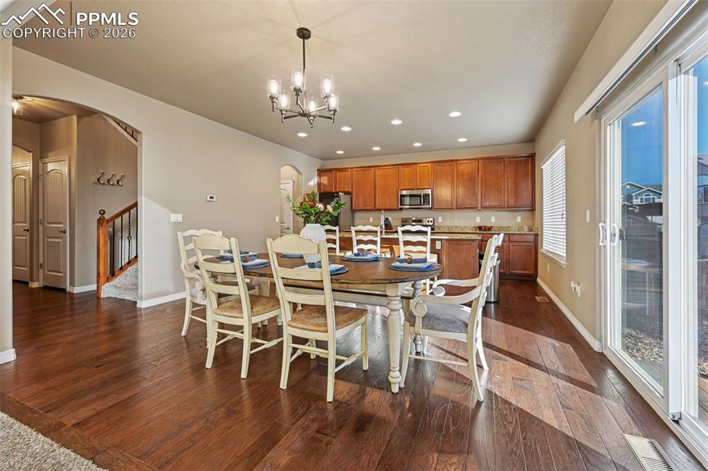 Image 14 of 38: Dining space with arched walkways, dark wood finished floors, and hanging l