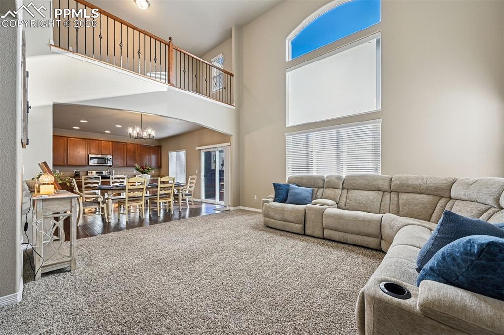 Image 15 of 38: Living area with dark colored carpet, a chandelier, arched walkways, and a