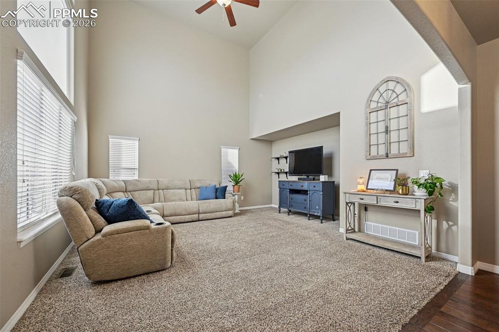 Image 17 of 38: Living room featuring ceiling fan, a high ceiling, and dark carpet