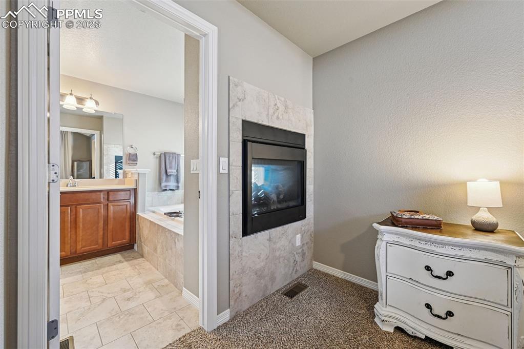 Image 23 of 38: Bathroom with vanity, a garden tub, light carpet, and a premium fireplace