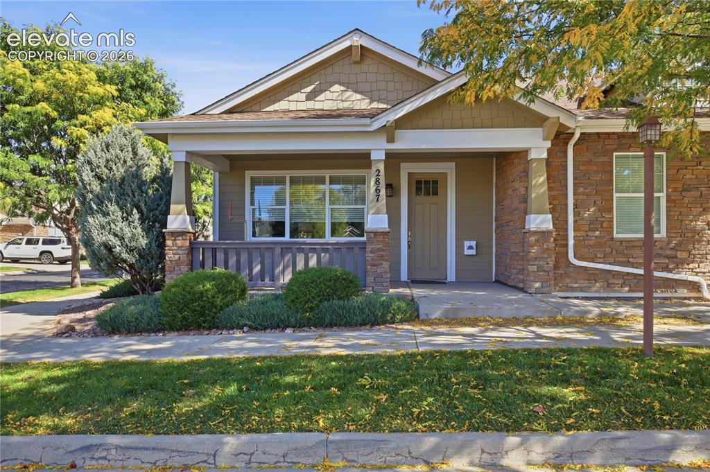 Caption: Exterior featuring a covered porch, stone accent columns, shake siding, and a paneled front door wit