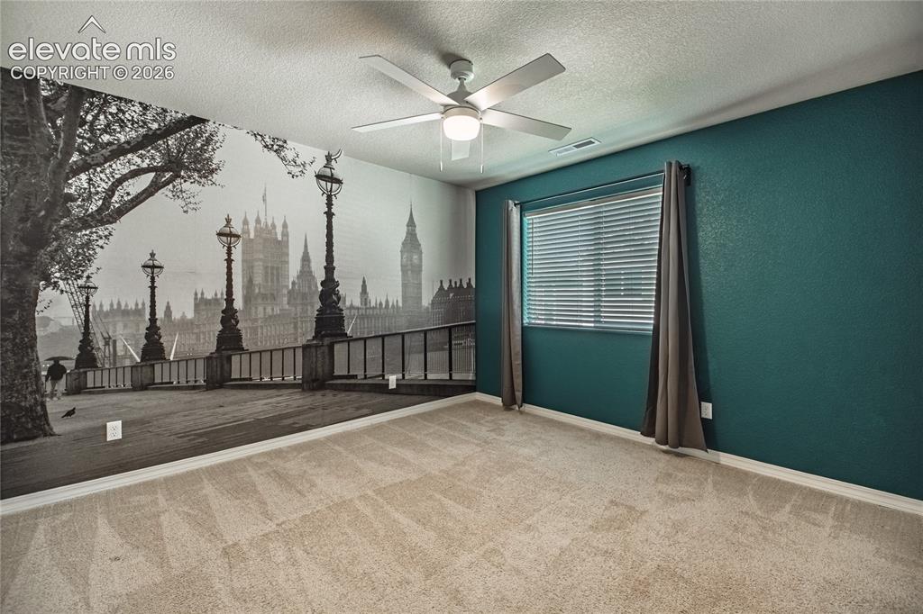 Image 23 of 35: Wall mural accent, deep teal painted walls, neutral carpet, ceiling fan, an