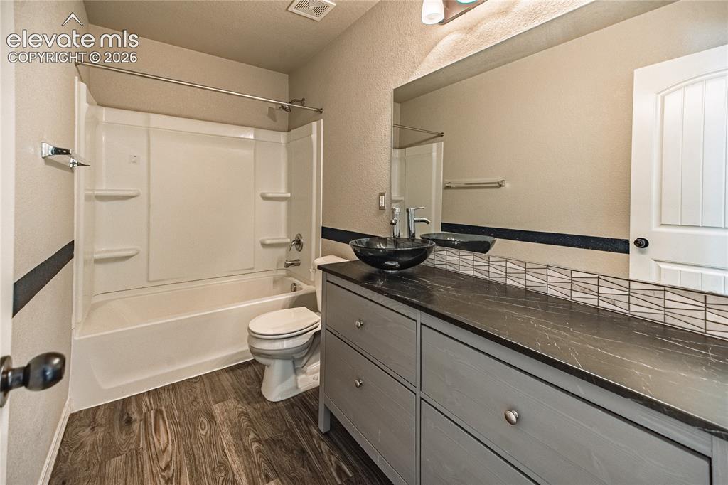 Image 27 of 35: Wood-finish flooring, full bathtub/shower combination, dark stone-finish co