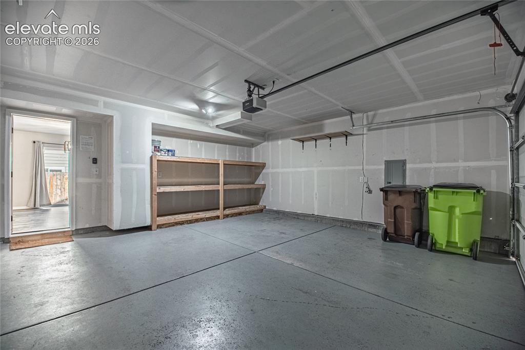 Image 29 of 35: Spacious garage with an overhead door, built-in shelving, and a concrete fl