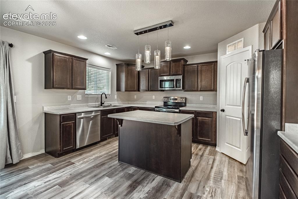 Image 5 of 35: Dark wood-finish cabinetry, stainless steel appliances, and a central islan