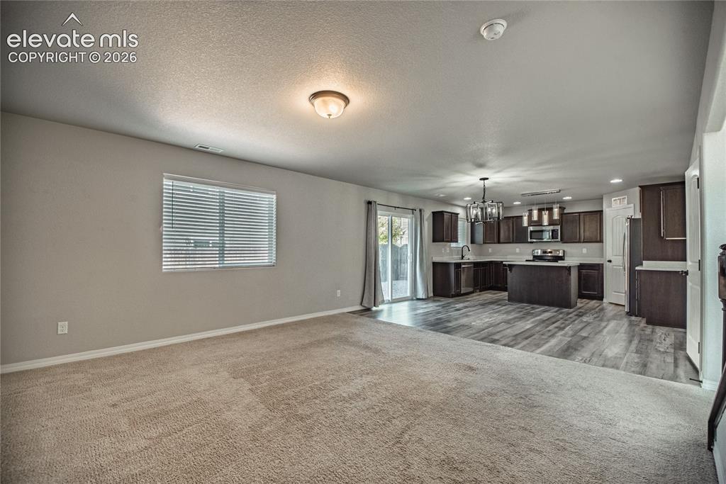 Image 8 of 35: Expansive living area with carpet flooring, window with blinds, and a built