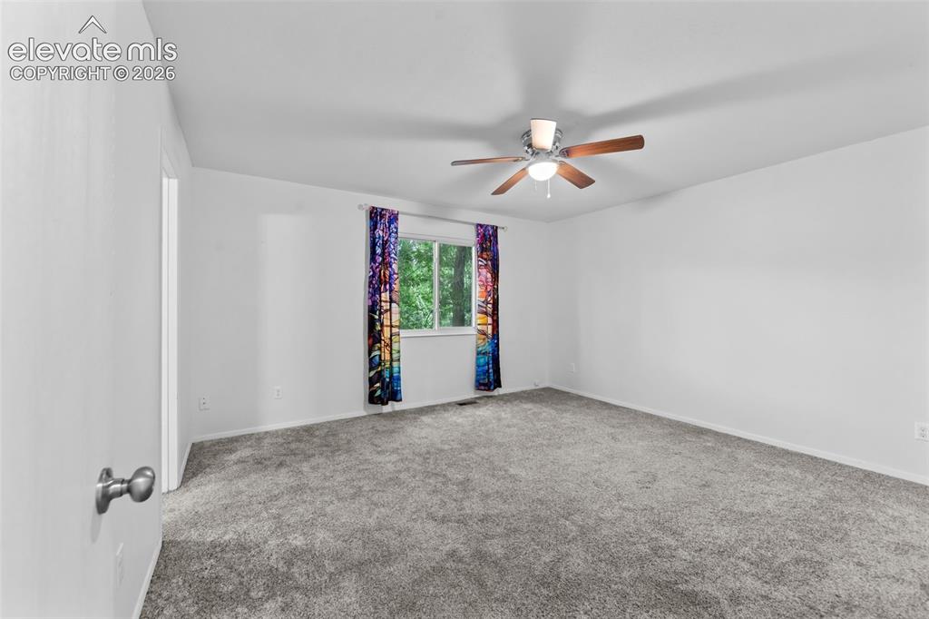 Image 13 of 20: Spacious room featuring neutral carpeting, a large window, and a ceiling fa