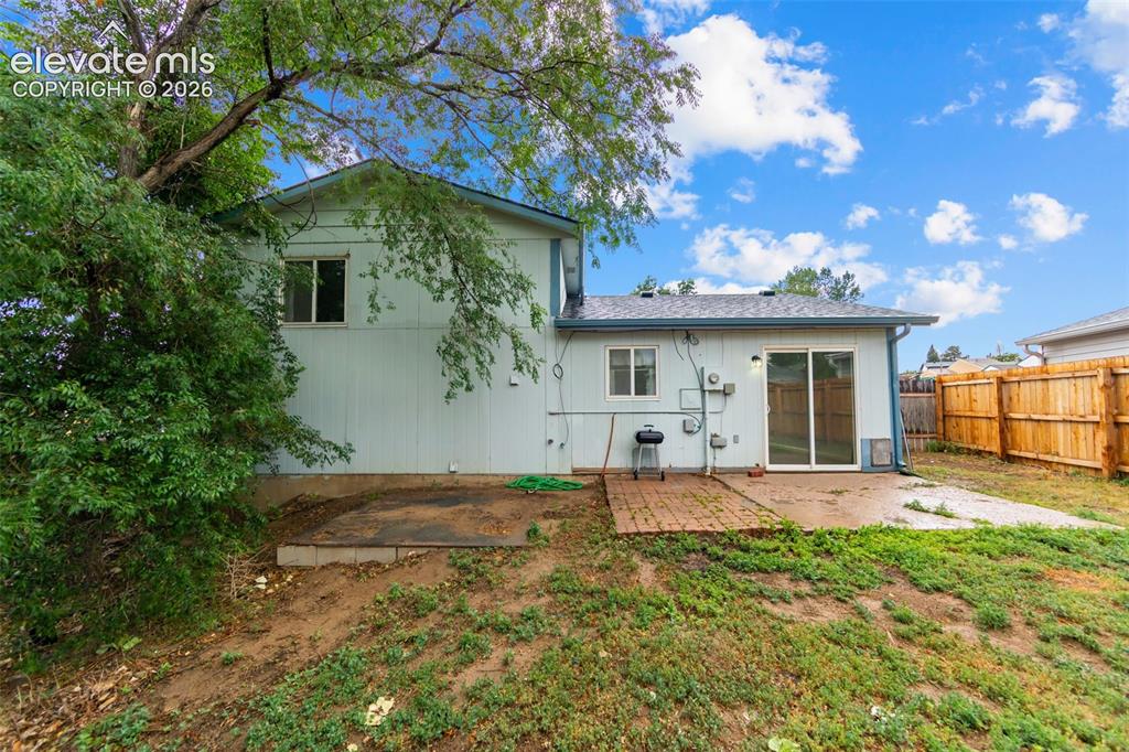 Image 18 of 20: Rear exterior featuring light-colored siding, a sliding glass door, a brick