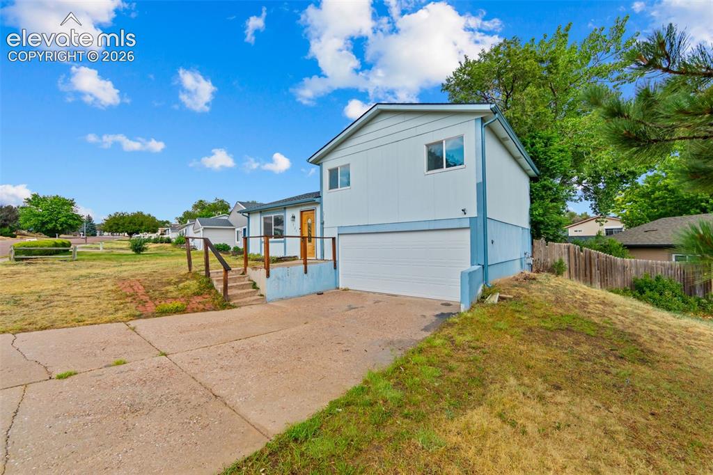 Image 2 of 20: Split-level residence featuring light-colored siding with blue trim accents