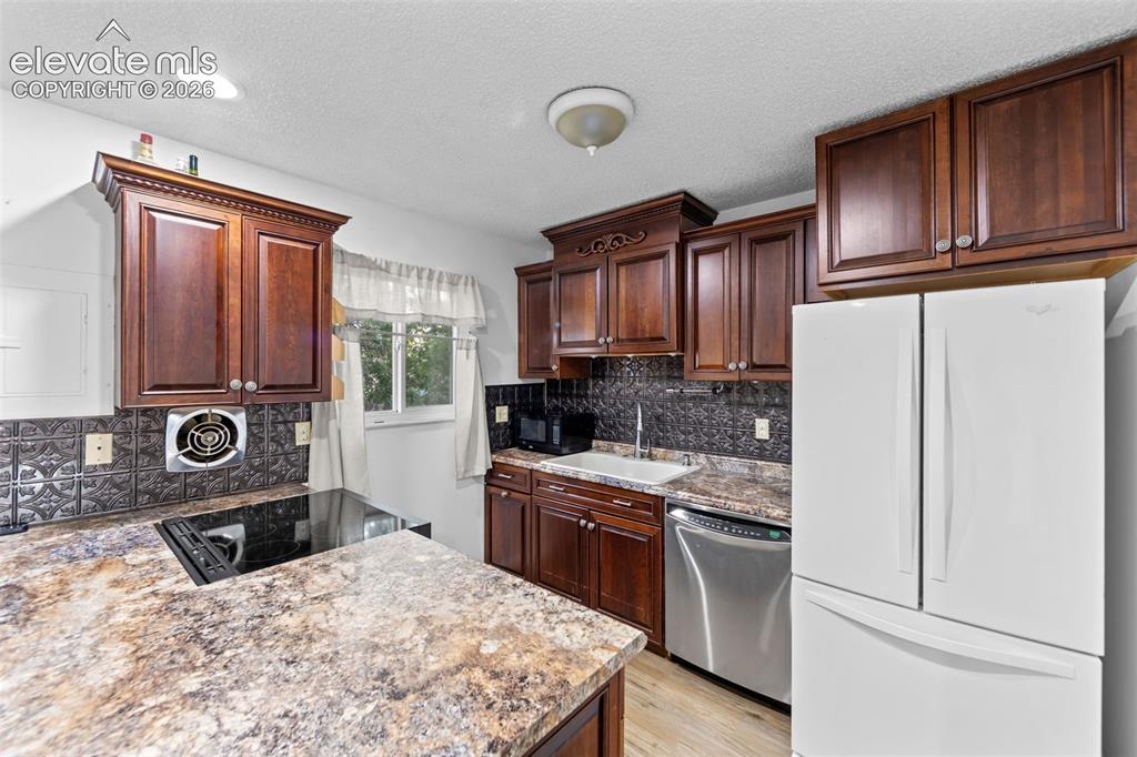 Image 8 of 20: Kitchen featuring dark wood cabinetry, patterned backsplash, integrated ele