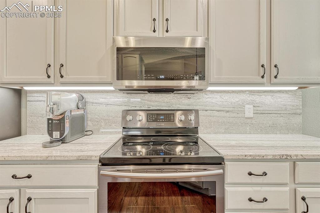 Image 12 of 41: Kitchen equipped with stainless steel appliances, backsplash, and white cab