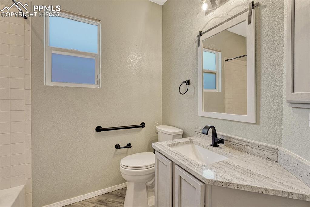 Image 5 of 41: This full bathroom features wood floors, a vanity, and textured walls.