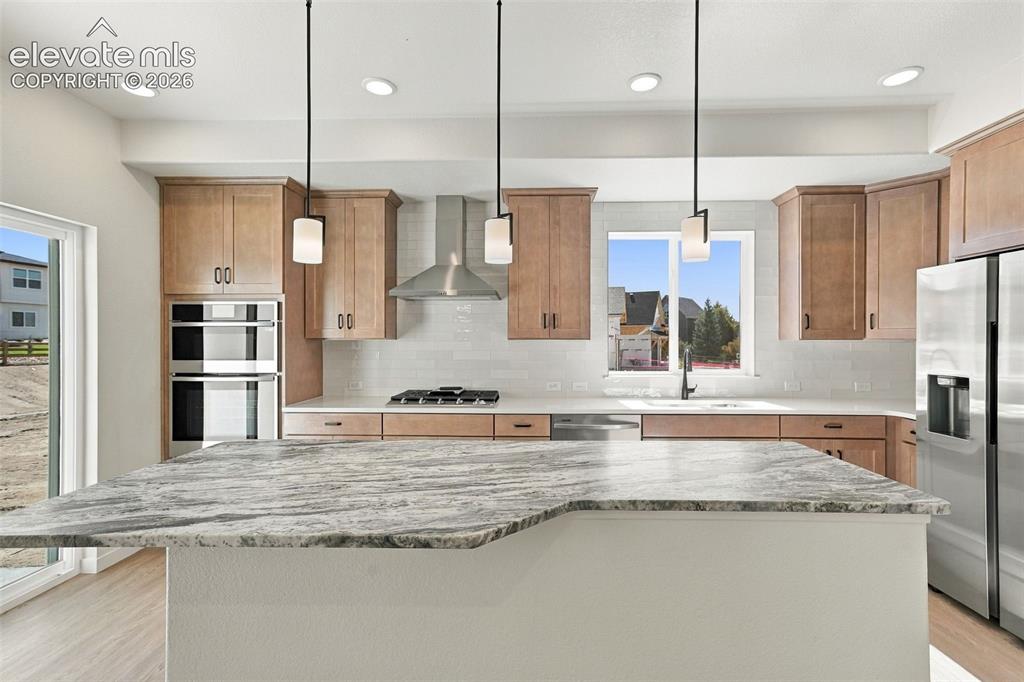 Image 15 of 49: Kitchen featuring a large island with a stone countertop, light wood-finish