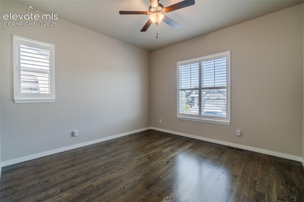 Image 17 of 50: Spacious room featuring wood-finish flooring, two windows with white louver