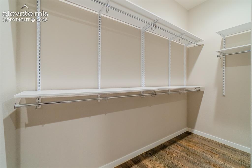 Image 21 of 50: Closet featuring adjustable shelving, multiple hanging rods, and wood-finis